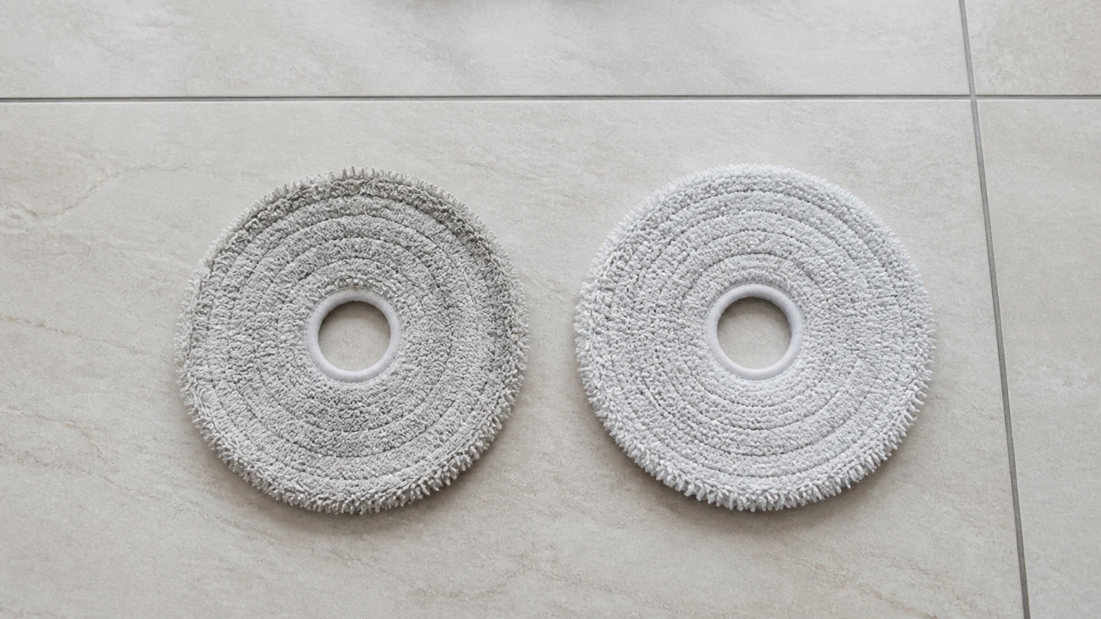 Pair of circular robot vacuum mop pads on a kitchen floor, worn pad beside a fresh replacement