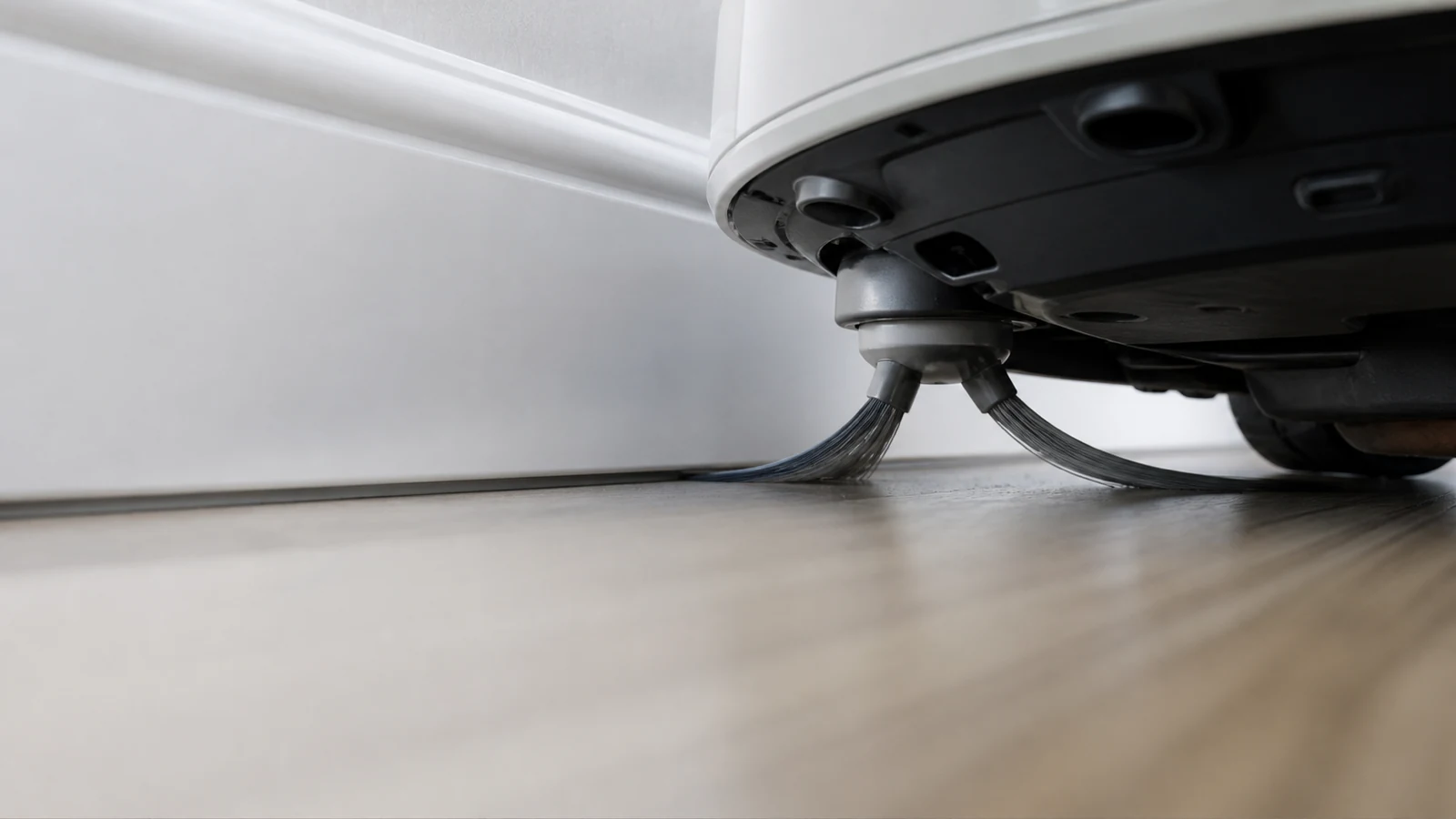 Robot vacuum side brush sweeping along a skirting board on a hard floor